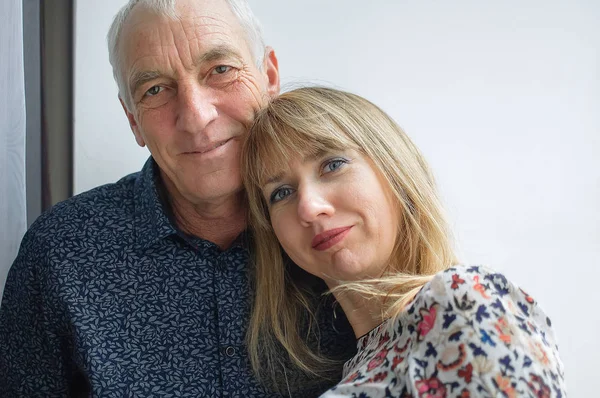 Precioso retrato romántico del anciano abrazando a su joven esposa de cabello rubio con un vestido cálido. Pareja con diferencia de edad . —  Fotos de Stock