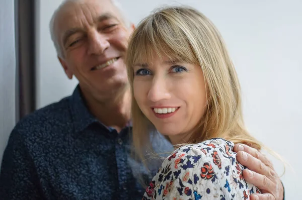 Sıcak elbise giyen genç sarı saçlı gülümseyen eşi sarılma yaşlı adam Lovely mutlu portre. Yaş farkı olan çift.