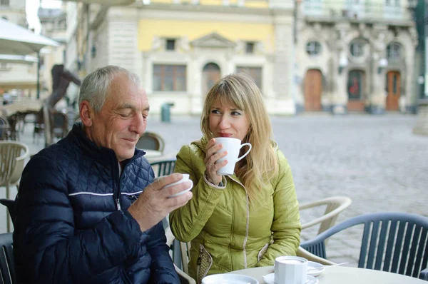 Mulher de meia-idade e seu marido idoso passar o tempo juntos ao ar livre sentado no café com terraço ao ar livre e beber café pela manhã durante o início da primavera ou outono — Fotografia de Stock