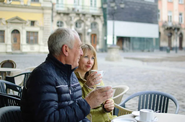 Двое туристов среднего возраста пьют кофе в кафе с террасой на свежем воздухе в древнем городе ранней весной или осенью — стоковое фото