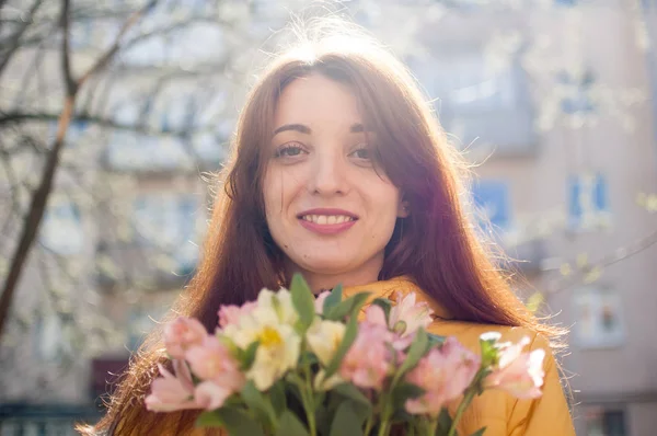 Retrato de mujer joven atractiva y hermosa en chaqueta amarilla sosteniendo un gran ramo de flores de colores al aire libre cerca de los edificios en el fondo —  Fotos de Stock