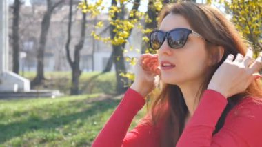 Kırmızı gömlekli çekici duygusal genç kız güneş gözlüğü çıkarıyor ve parkta açık havada sürpriz harcama ile kameraya bakıyor