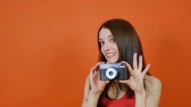 Elinde kamera olan güzel genç kahverengi saçlı kız. Duyguları. Turuncu arka plan üzerine bir stüdyoda sanat portresi
