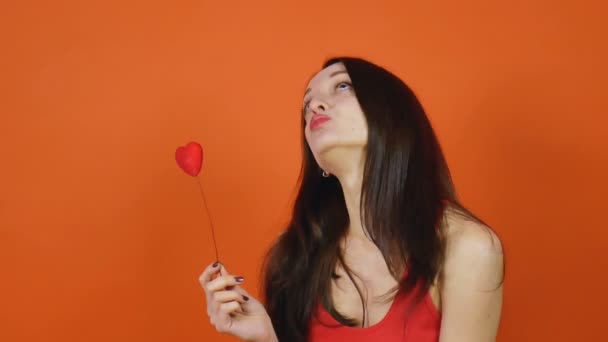 Young beautiful brown-haired girl with a valentine heart on an orange background. Artportret — Stock Video