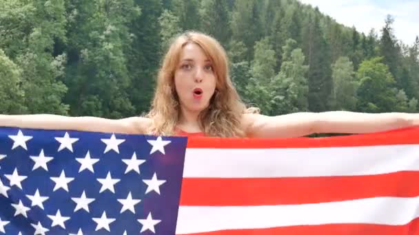 Патріотичне свято. Щаслива емоційна жінка з американським прапором на зеленому тлі лісу в літній день на відкритому повітрі. США відзначають 4 липня. — стокове відео