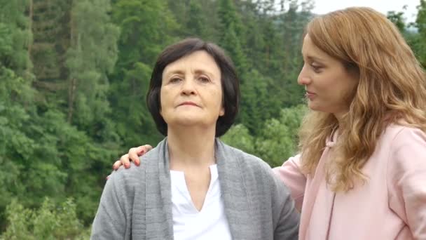 Outdoor close up portrait of smiling happy caucasian senior mother with her adult daughter hugging and looking at the camera. Adult daughter kisses mother, mothers day — Stock Video