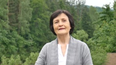Dağ ormanının arka planında güzel yaşlı kadın eliyle saçlarını düzleştiriyor. Emekliler seyahat, mutlu yaşlılık, sosyal kavram, anneler günü
