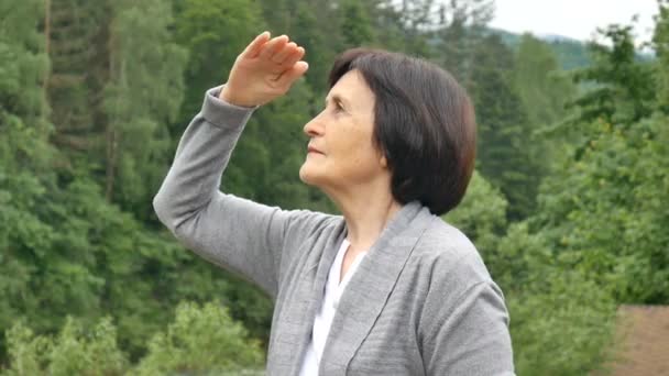 Donna bruna matura guarda in lontananza in montagna e agita la mano, un gesto di saluto. Vacanze estive, viaggi in pensione — Video Stock