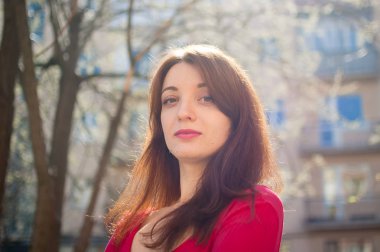 Kırmızı gömlekli, şehvetli dudakları olan genç esmer kadın güneş parlarken açık havada bahar esintisinin tadını çıkarıyor.