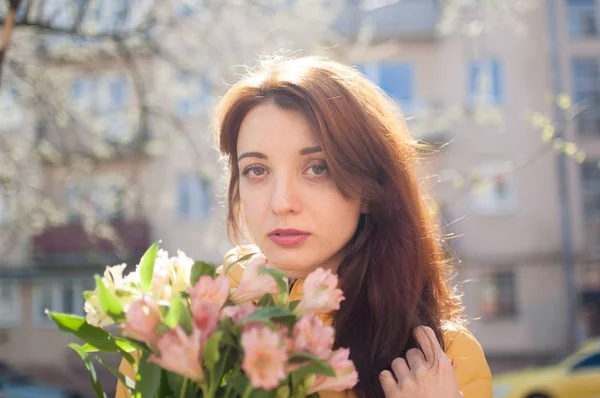 Sensual chica joven mirando a la cámara y sosteniendo un gran ramo de flores de colores al aire libre cerca de los edificios en el fondo — Foto de Stock