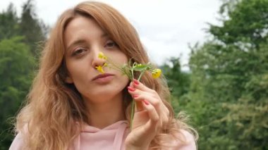 Sarı bir yabani çiçek tutan güzel kıvırcık kızıl saçlı kadın. Orman ve dağlara karşı portre. Yaz tatili, bahar tazeliği, anneler günü, alerji ücretsiz