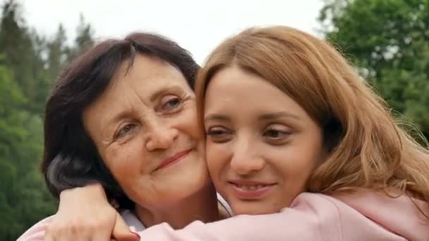 Закрыть портрет улыбающейся счастливой старшей матери-кавказки со взрослой дочерью, обнимающейся и смотрящей в камеру. Взрослая дочь целует мать, День матери — стоковое видео