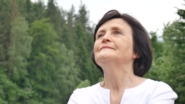 Senior woman doing a stretching exercise for the upper arms outside over landscape of forest and mountains — Stock Video