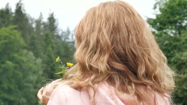 Mulher ruiva encaracolada bonita segurando uma flor selvagem amarela. Retrato contra a floresta e montanhas. Férias de verão, frescura primavera, dia das mães, livre de alergias — Vídeo de Stock