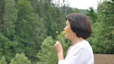Elinde kır çiçekleri olan bir dağ ormanının arka planında yaşlı ve güzel bir kadının yakın çekim portresi