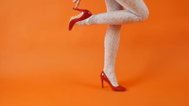 Hermosas piernas femeninas con tacones altos rojos y medias de rejilla blanca sobre fondo naranja. Estilo retro — Vídeos de Stock