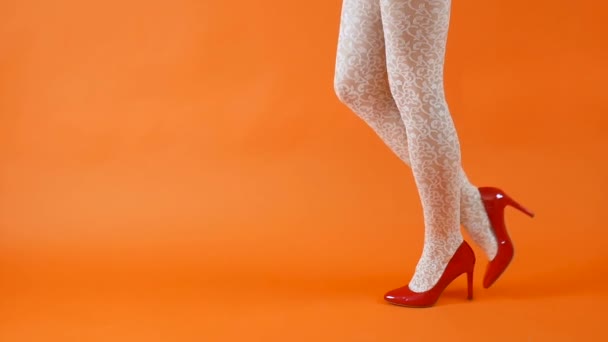 Sexy piernas largas en zapatos de tacón alto rojo y medias de rejilla blanca sobre fondo naranja. Estilo retro — Vídeos de Stock