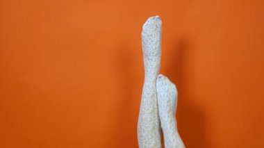 Parlak turuncu arka planda beyaz file tayt güzel genç kadının Bacakları