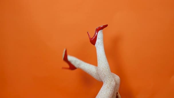 Sexy piernas largas en zapatos de tacón alto rojo y medias de rejilla blanca sobre fondo naranja. Estilo retro — Vídeo de stock