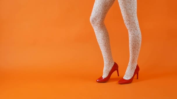 Beautiful female legs with red high heels and white fishnet stockings on orange background. Retro style — Stock Video