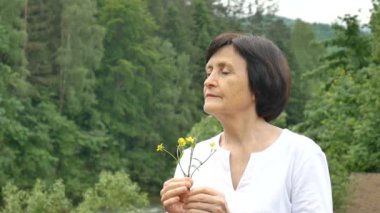 Elinde kır çiçekleri olan bir dağ ormanının arka planında yaşlı ve güzel bir kadının yakın çekim portresi