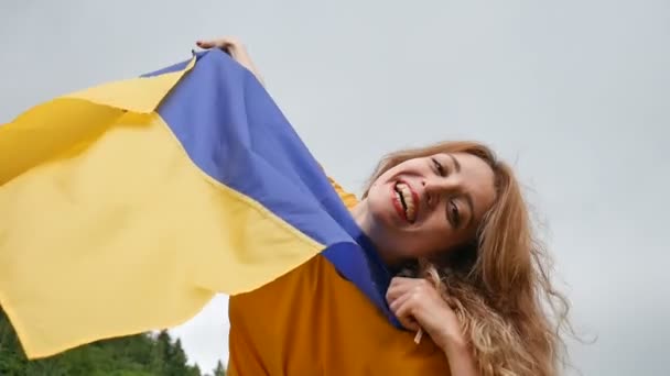 Retrato femenino exterior de una joven patriótica sosteniendo una bandera azul y amarilla de Ucrania sobre el fondo del cielo — Vídeo de stock