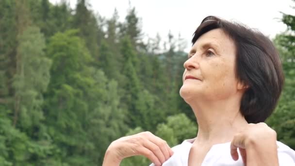 Senior woman doing a stretching exercise for the upper arms outside over landscape of forest and mountains — Stock Video