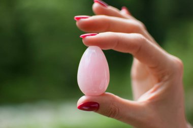 Yoni yumurtası tutan kadın elin yakın fotoğrafı. Nehir arka plan üzerinde gül kuvars kristal yumurta. Kadın sağlığı kavramı