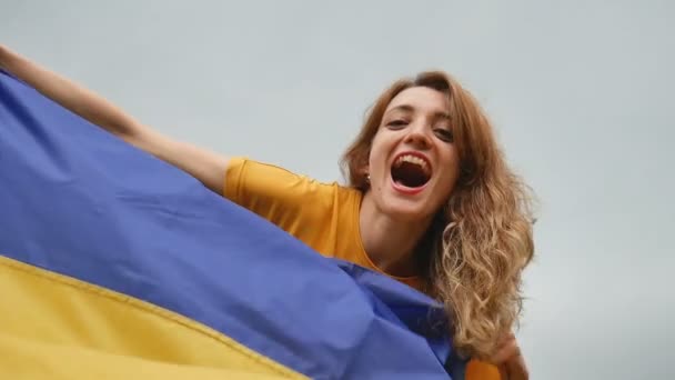 Emotionele jonge vrouw Holding blauwe en gele Oekraïense vlag over de hemel achtergrond — Stockvideo