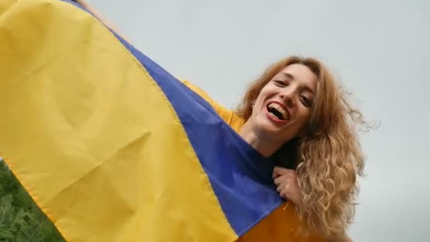 Retrato al aire libre de niña riendo con bandera ucraniana azul y amarilla en sus manos sobre el fondo del cielo — Vídeos de Stock