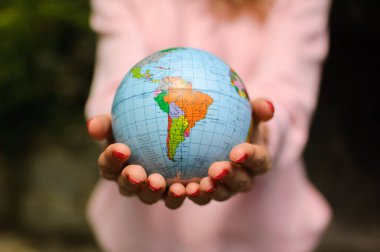 Kırmızı manikür ile pembe bir kazak kız üzerinde Ukrayna kiril harfleri geografical isimleri ile küçük bir küre tutar. Güney Amerika görülebilir. Ekolojik sorunlar kavramı.