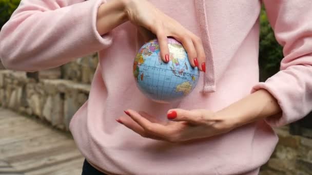 Young female teenager in pink casual clothes with red manicure holding a little globe with geografical names in Ukrainian cyrillic letters on it in her hands. Enviromental responsibility concept. — Stock Video