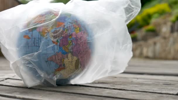 Side view of the Earth in polyethylene disposable package on wooden background. Concept of ecological problems. Stop garbage pollution — Stock Video