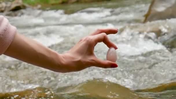 Mano femminile che tiene un uovo di cristallo di quarzo rosa yoni sullo sfondo del fiume. Salute delle donne, unità con i concetti di natura . — Video Stock