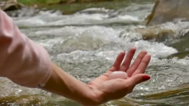 Samičí ruka držící na pozadí řeky růžovou křemennou krystalku. Zdraví, jednota, koncepce přírody. — Stock video