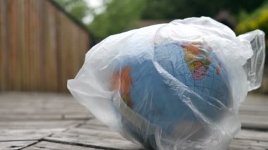 Ahşap arka planda polietilen tek kullanımlık paket Earth yan görünümü. Ekolojik sorunlar kavramı. Çöp kirliliğini durdurma