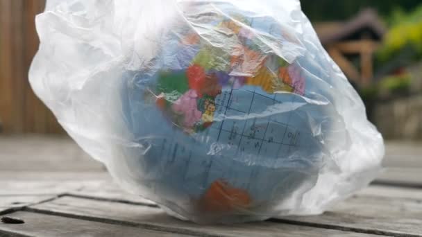 Zijaanzicht van de wereldbol van de aarde in polyethyleen wegwerp pakket op houten achtergrond. Concept van ecologische problemen. Vuil vervuiling stoppen — Stockvideo