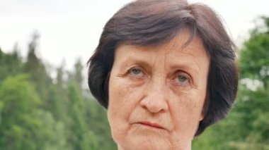 Arka planda yeşil orman ile dağ tepeüzerinde yüzünde kısa koyu saçlı ve kırışıklıkları ile düşünceli üzgün yaşlı kadın Portresi