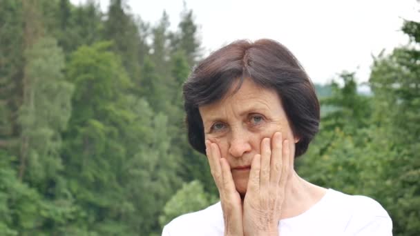Kısa koyu saçlı ve kırışık yüzü yeşil orman arka plan üzerinde üzüntü ile kameraya bakarak yaşlı bir kadının Açık hava portresi — Stok video