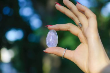 Vumfit, imbuilding veya meditasyon için şeffaf ametist kuvars yoni yumurta ile Kadın el. Gün doğumu arka planda açık havada ellerde parlayan kristal yumurta. Doğa kavramı ile kadın sağlığı ve birliği
