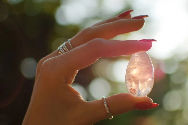 Female hand with transparent amethyst quartz yoni egg for vumfit, imbuilding or meditation. Shining crystal egg in hands on sunrise background outdoors. Womens healthand unity with the nature concept