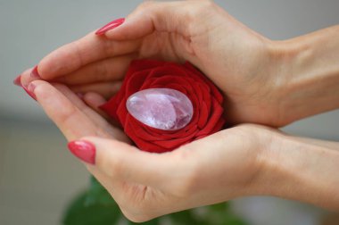 Bir yoni yumurta ve kırmızı gül tutan kadın el kapalı fotoğraf. Adet sembolü olarak çiçek. Adet krampları sırasında vumfit, imbuilding veya meditasyon için şeffaf menekşe ametist kristal