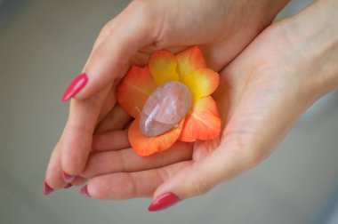 Vumfit için şeffaf menekşe ametist yoni yumurta tutan kırmızı manikür ile Kadın el, turuncu ve sarı gladiolus çiçek içinde imbuilding veya meditasyon.
