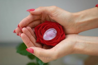 Manikür lü kadın elleri yoni yumurtası ve kırmızı gül tutuyor. Adet sembolü olarak çiçek. Adet krampları sırasında vumfit, imbuilding veya meditasyon için şeffaf menekşe ametist kristal
