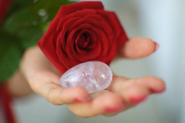 Manikür lü kadın elleri yoni yumurtası ve kırmızı gül tutuyor. Adet sembolü olarak çiçek. Adet krampları sırasında vumfit, imbuilding veya meditasyon için şeffaf menekşe ametist kristal