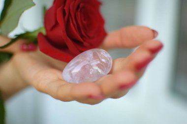 Manikür lü kadın elleri yoni yumurtası ve kırmızı gül tutuyor. Adet sembolü olarak çiçek. Adet krampları sırasında vumfit, imbuilding veya meditasyon için şeffaf menekşe ametist kristal