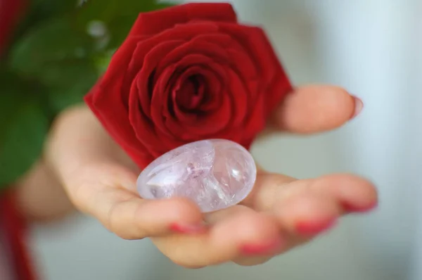 Female hands with manicure holding a yoni egg and red rose. The flower as a symbol of menstruation. Transparent violet amethyst crystal for vumfit, imbuilding or meditation during menstrual cramps — Stock Photo, Image