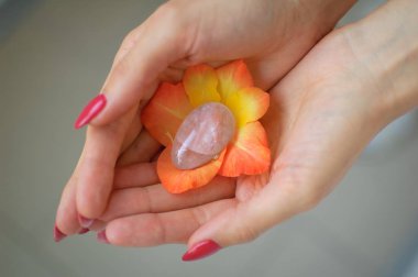 Vumfit için şeffaf menekşe ametist yoni yumurta tutan kırmızı manikür ile Kadın el, turuncu ve sarı gladiolus çiçek içinde imbuilding veya meditasyon.