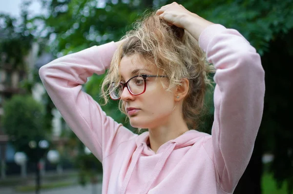 Portrait extérieur de fille blonde avec des lunettes hipster en vêtements roses faisant queue de cheval à l'extérieur dans le parc urbain — Photo