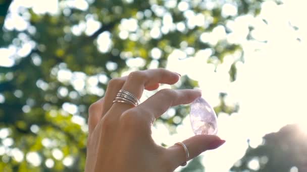 Ženská ruka s průhledným ametystovým vajíčkem pro zumvání, nebudování nebo meditaci. Zářící křišťálové vajíčko v ruce na obloze a v pozadí východu slunce venku. Zdravotní koncepce. — Stock video